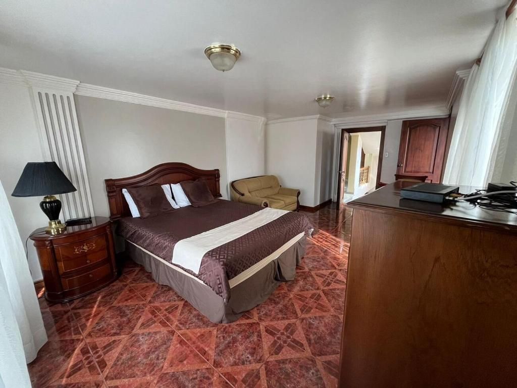 A hotel room with a bed, a chair, a desk, and a lamp.