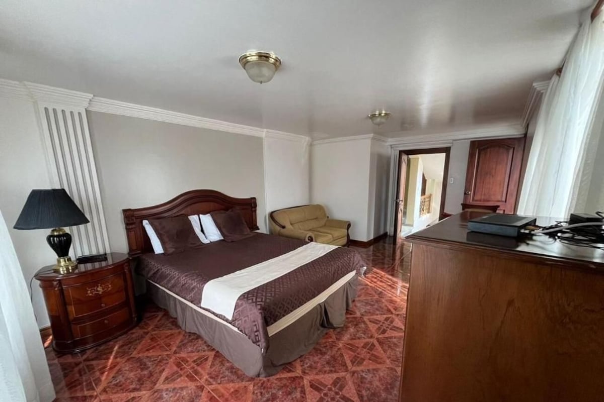 A hotel room with a bed, a chair, a desk, and a lamp.