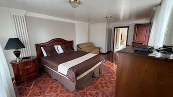 A hotel room with a bed, a chair, a desk, and a lamp.