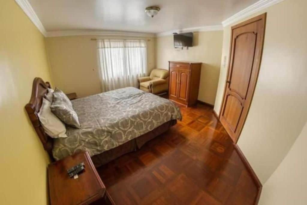 A bedroom with a bed, a chair, a wardrobe, and a television on the wall.