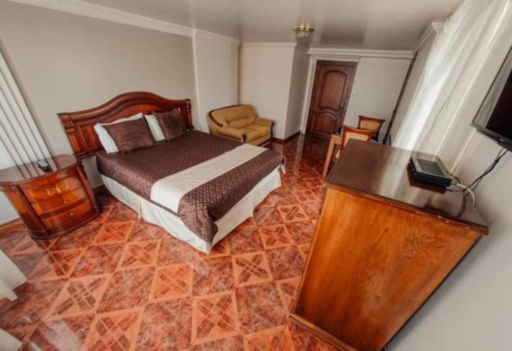A hotel room with a bed, a wooden nightstand, a chair, a desk, and a television.