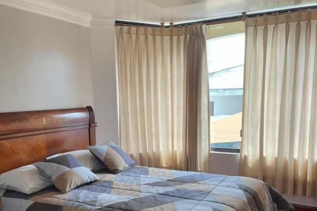 A bedroom with a wooden headboard, a large bed with a checkered bedspread, and a window with curtains.