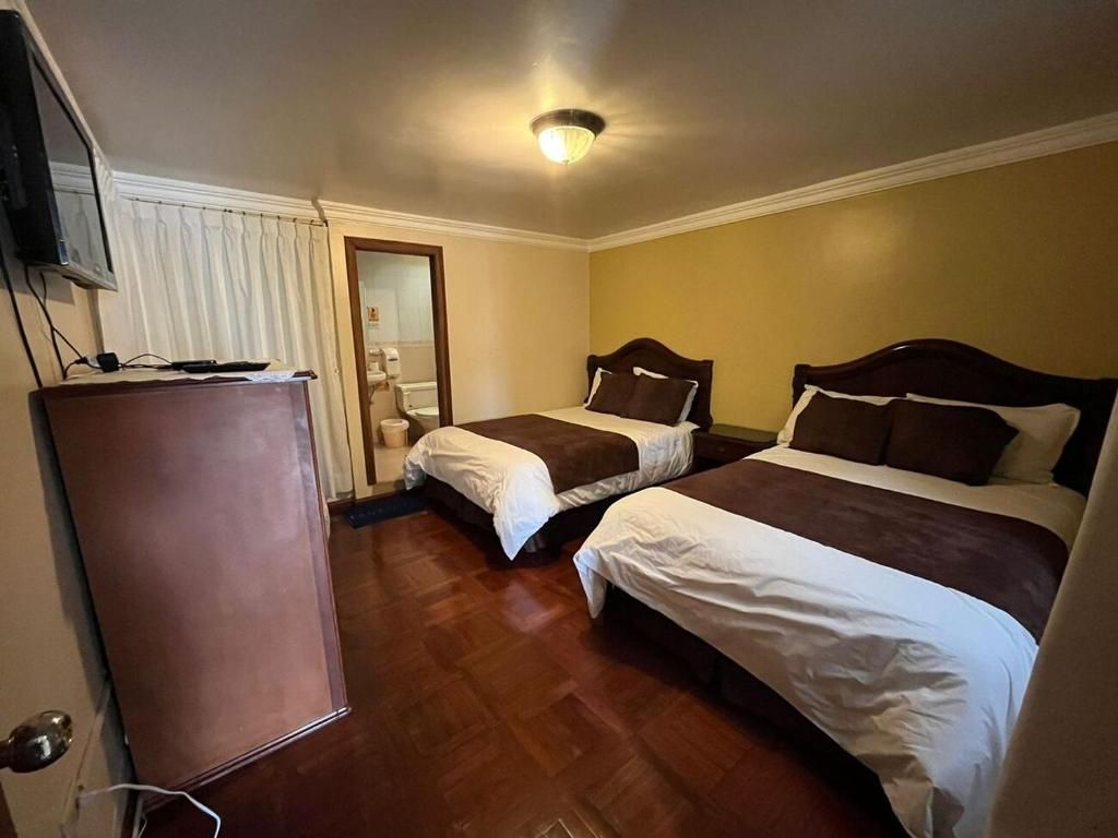 A hotel room with two beds, a television, and a wooden floor.