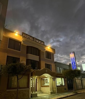 Ein Hotel namens 'HOTEL ROCIO' mit auffälliger Beschilderung, überdachter Eingangsparte und gut beleuchteter Fassade.
