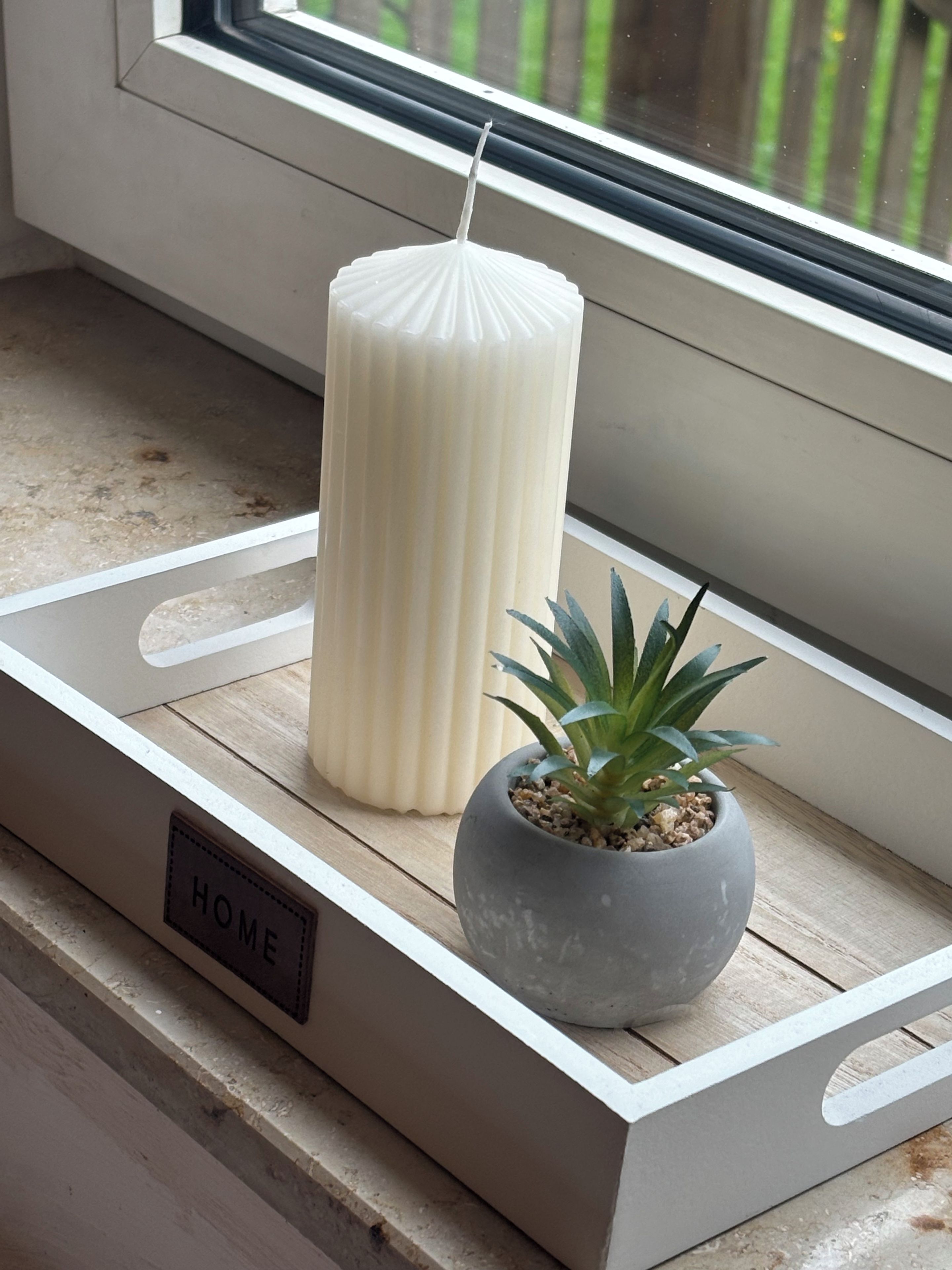 A window sill with a white candle, a potted plant, and a 'HOME' sign.
