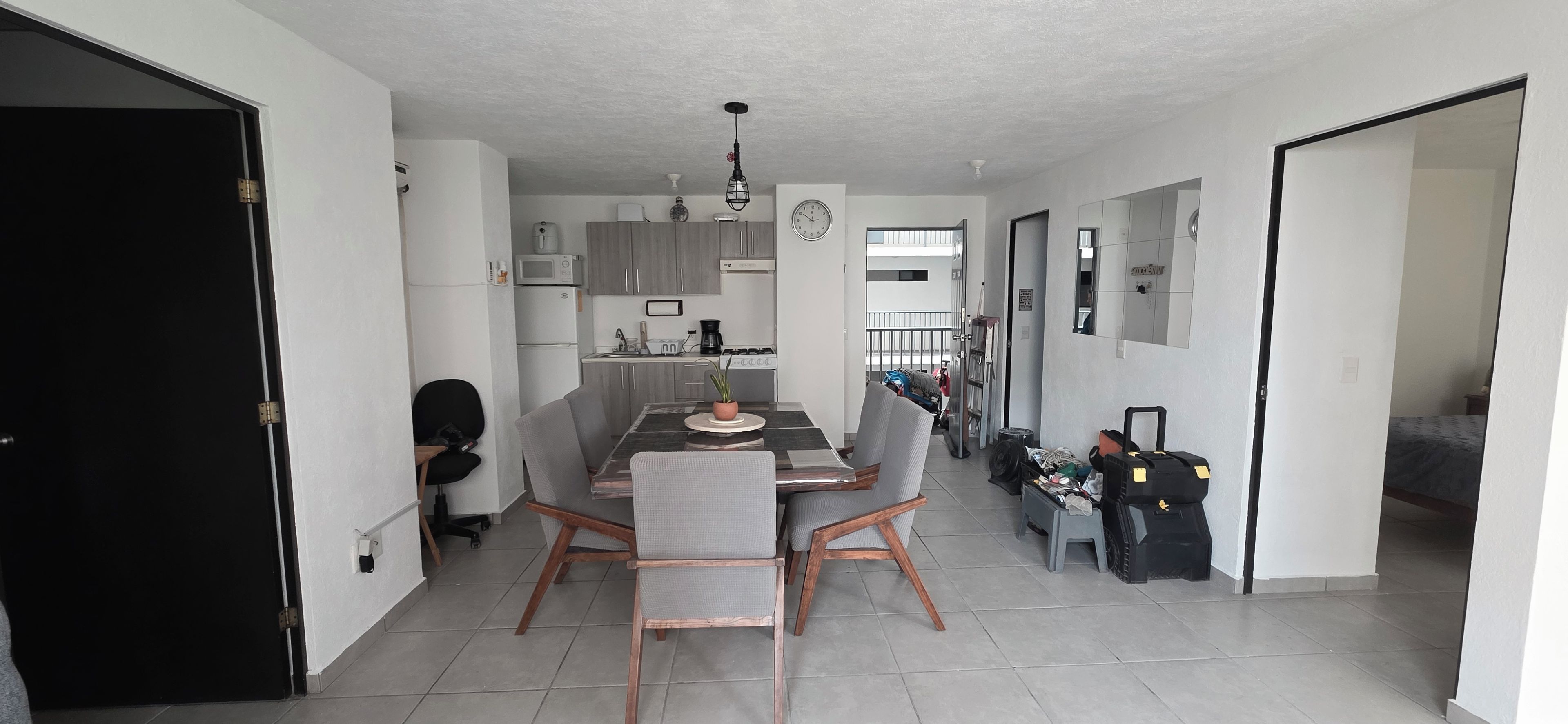 A modern kitchen with grey cabinets, a dining table with chairs, and a visible clock on the wall.