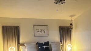 Un dormitorio con cama, lámparas de noche, ventilador de techo, una lámpara de pared y alfombra.