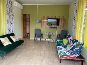 Un salon avec un canapé vert, un canapé aux couleurs vives, une petite table et un téléviseur fixé au mur.