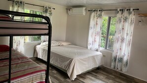 Een kamer met een stapelbed, een eenpersoonsbed, een raam met gordijnen en een airconditioning.