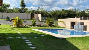 A swimming pool with a stone wall and palm trees in a landscaped yard. - Private Oasis Villa: Pool, BBQ Area & Lush Nature - Family Friendly (Provincia de Panamá Oeste, Corregimiento de Guayabito)