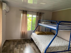A bunk bed room with a window, curtains, and an air conditioning unit.