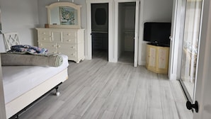 Et soveværelse med seng, kommode, fjernsyn og en skydedør til et badeværelse.