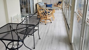 En overdækket patio med spisebord og stole, ventilator i loftet og store vinduer.
