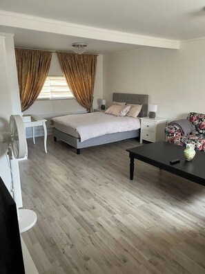 Une chambre à coucher comprenant un lit, des tables de chevet, un bureau, une chaise, un ventilateur et une table avec un vase.