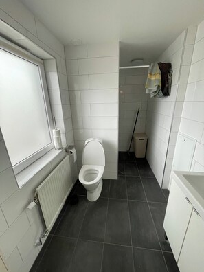 Une petite salle de bain avec des toilettes, un radiateur, une fenêtre et une serviette accrochée au mur.