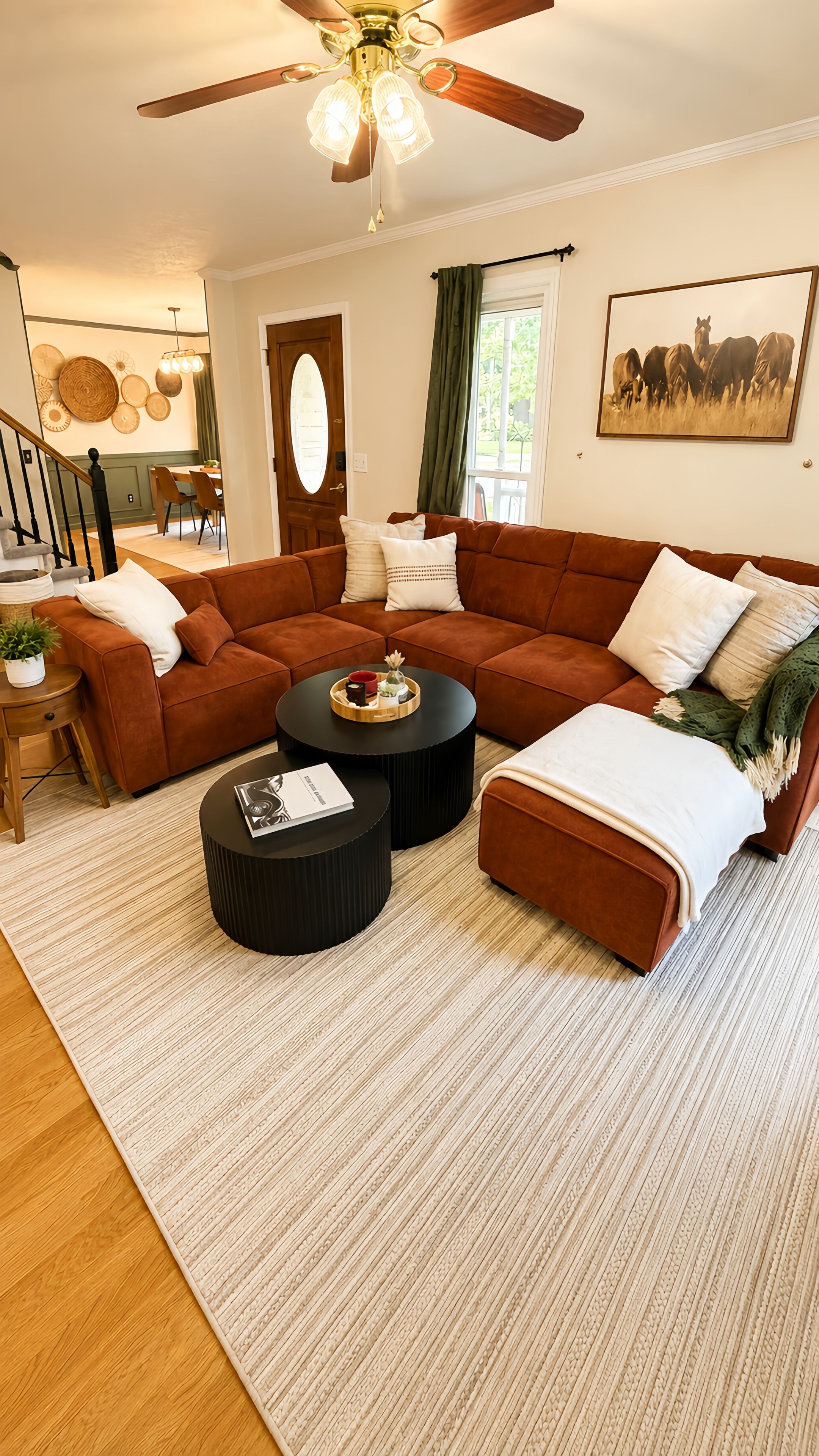 Ein Wohnzimmer mit braunen Sofas, zwei schwarzen Couchtischen, Holzboden und Deckenventilator.