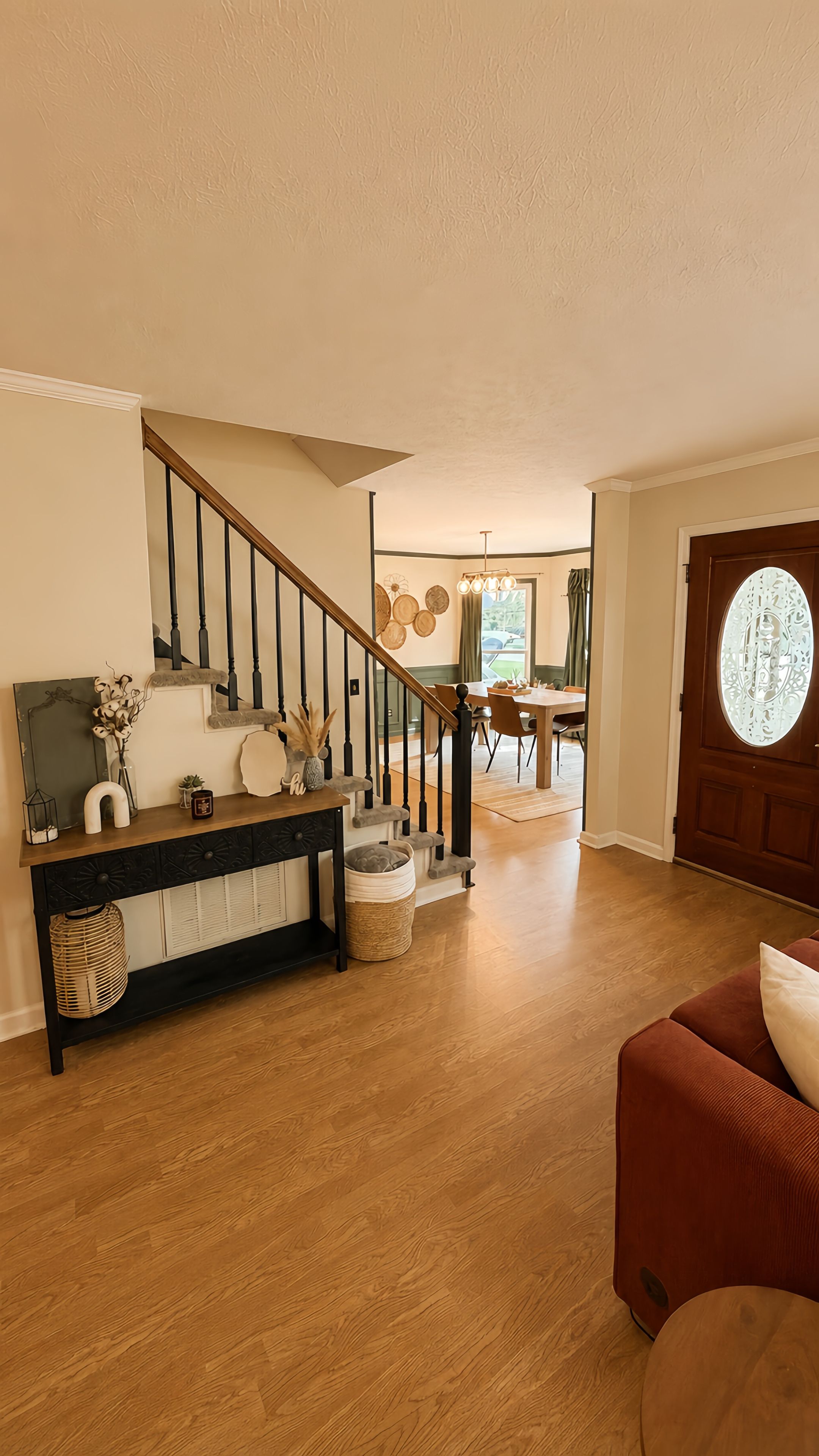 A spacious living area with a wooden staircase, a dining table, and a red sofa.
