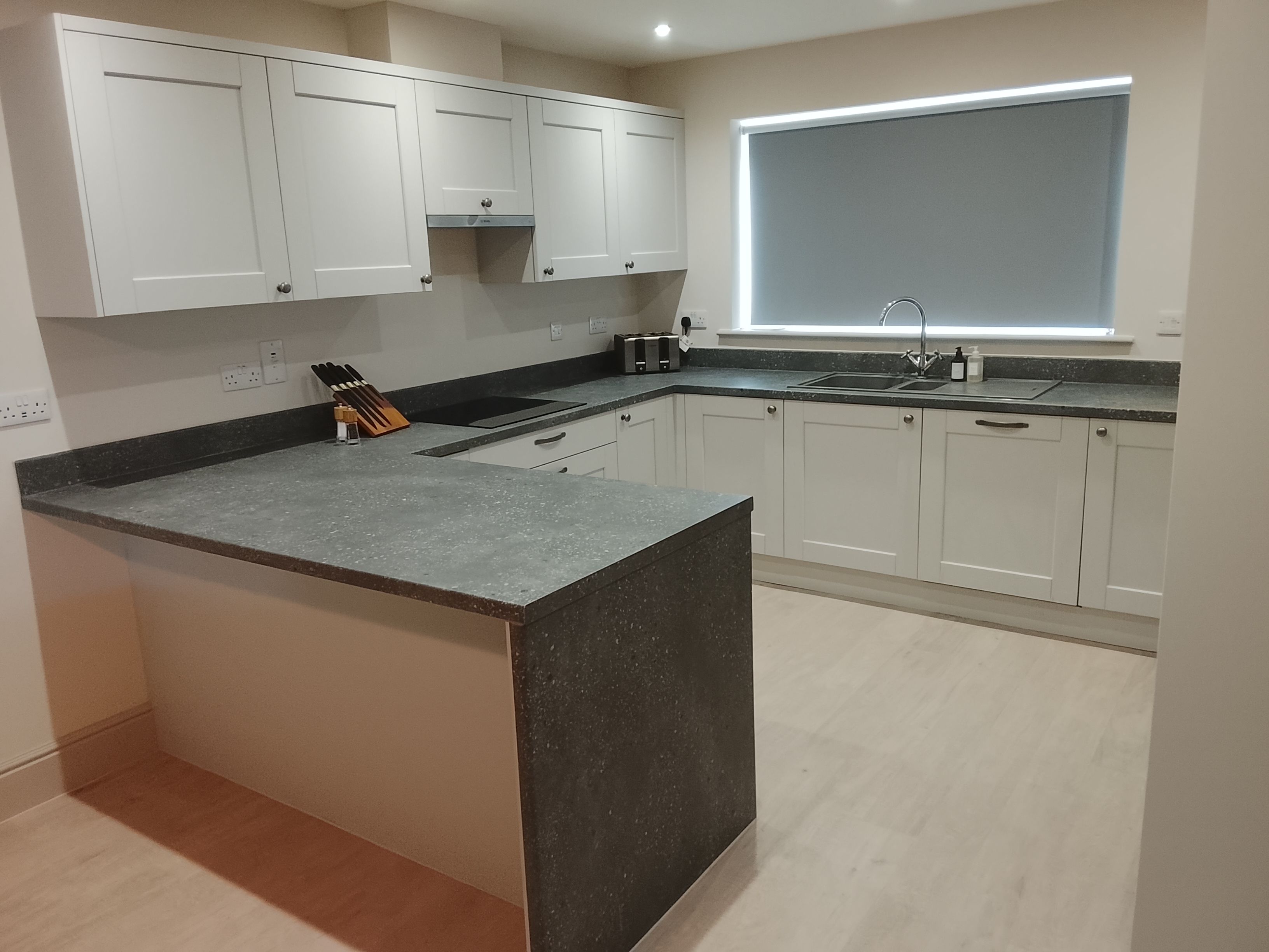 Una cocina moderna con armarios blancos, encimera de granito y ventana con persianas.