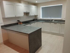 A modern kitchen with white cabinets, a granite countertop, and a window with blinds. - Village House with open countyside views close by the bustling 'Norton Dog ' pub (Norton)