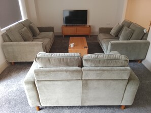 Una sala de estar con un juego de sofá, una mesa de centro y un televisor sobre un mueble de madera.