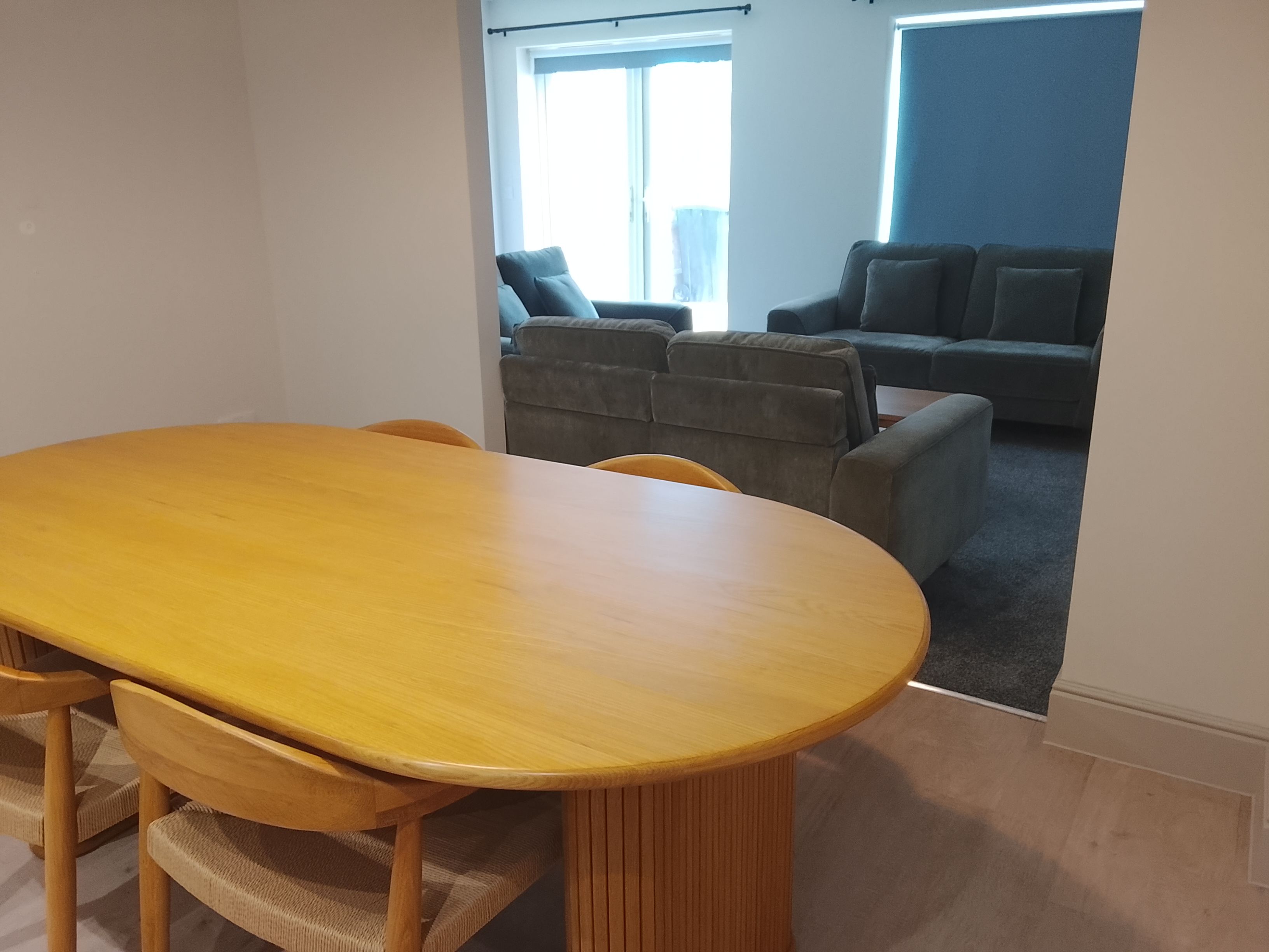 Un comedor con una mesa y sillas de madera, un sofá y una ventana con cortinas.