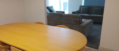 A dining area with a wooden table and chairs, a sofa, and a window with curtains.