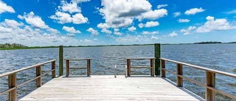 Un muelle de madera que se adentra en el agua, con un banco en el centro y barandillas a ambos lados.