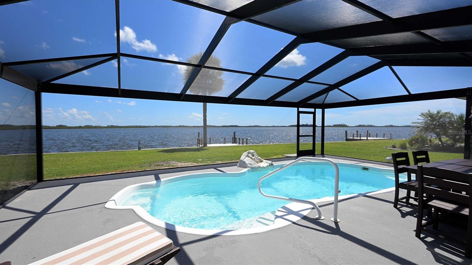 Een zwembad met uitzicht op een waterpartij, een overdekt zitgedeelte en een kleine hottub.
