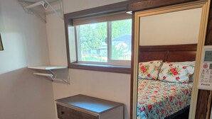 Un dormitorio con un aparador de madera, una cama con ropa de cama floral, una ventana con vistas y un espejo con reloj digital.