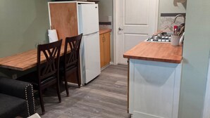 Cocina compacta con refrigerador, microondas y estufa, zona de comedor con mesa y sillas, y un pequeño rincón de descanso con sofá y sillón.