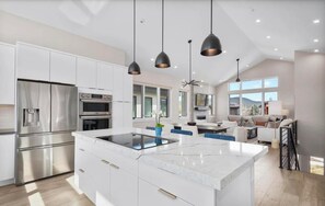 Une cuisine moderne dotée d’un îlot central, d’appareils électroménagers intégrés et de luminaires suspendus.