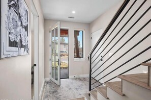 Un interior moderno con una escalera, una puerta de cristal que da al exterior y una obra de arte colgada en la pared.
