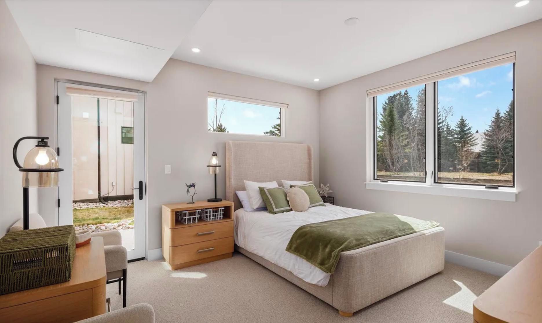 Un dormitorio con cama, mesita de noche, lámpara y ventana con vistas a árboles.