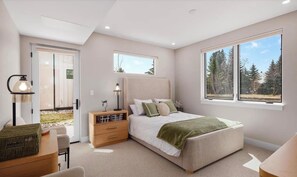 Une chambre moderne comprenant un lit, des tables de chevet, une lampe, une fenêtre donnant sur un paysage arboré et une porte menant à un espace extérieur.