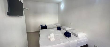 A single bed with white bedding and two pillows, a bedside table with a lamp, and a flat-screen TV mounted on the wall.