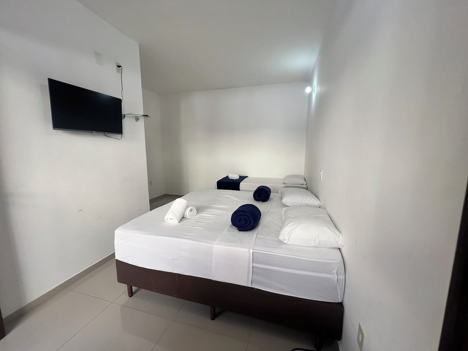 A hotel room with a bed, a flat-screen TV mounted on the wall, and a small table with a towel.