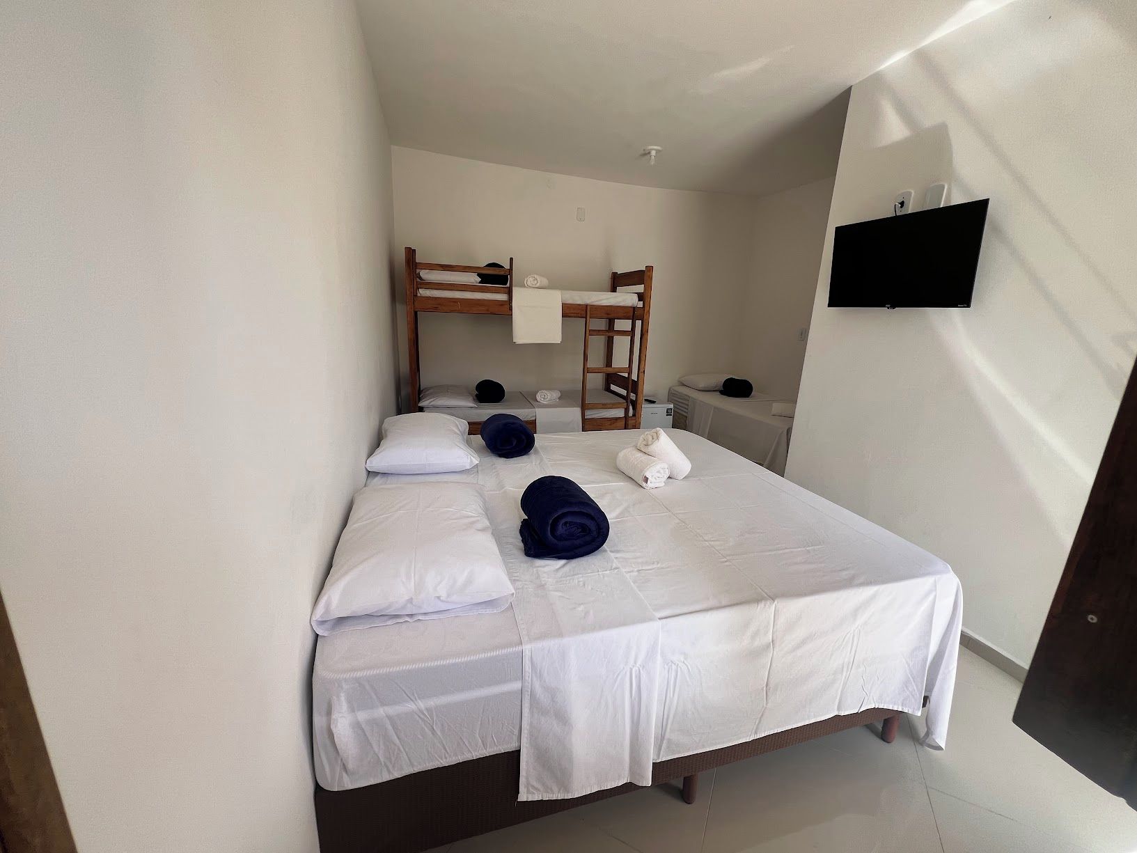 Una cama individual con ropa blanca, cabecera de madera y una mesita de noche con una lámpara.