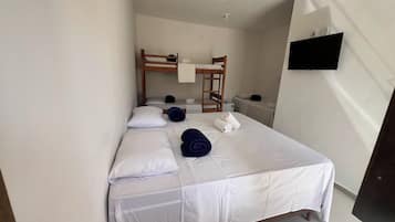 Una cama individual con ropa blanca, cabecera de madera y una mesita de noche con una lámpara.
