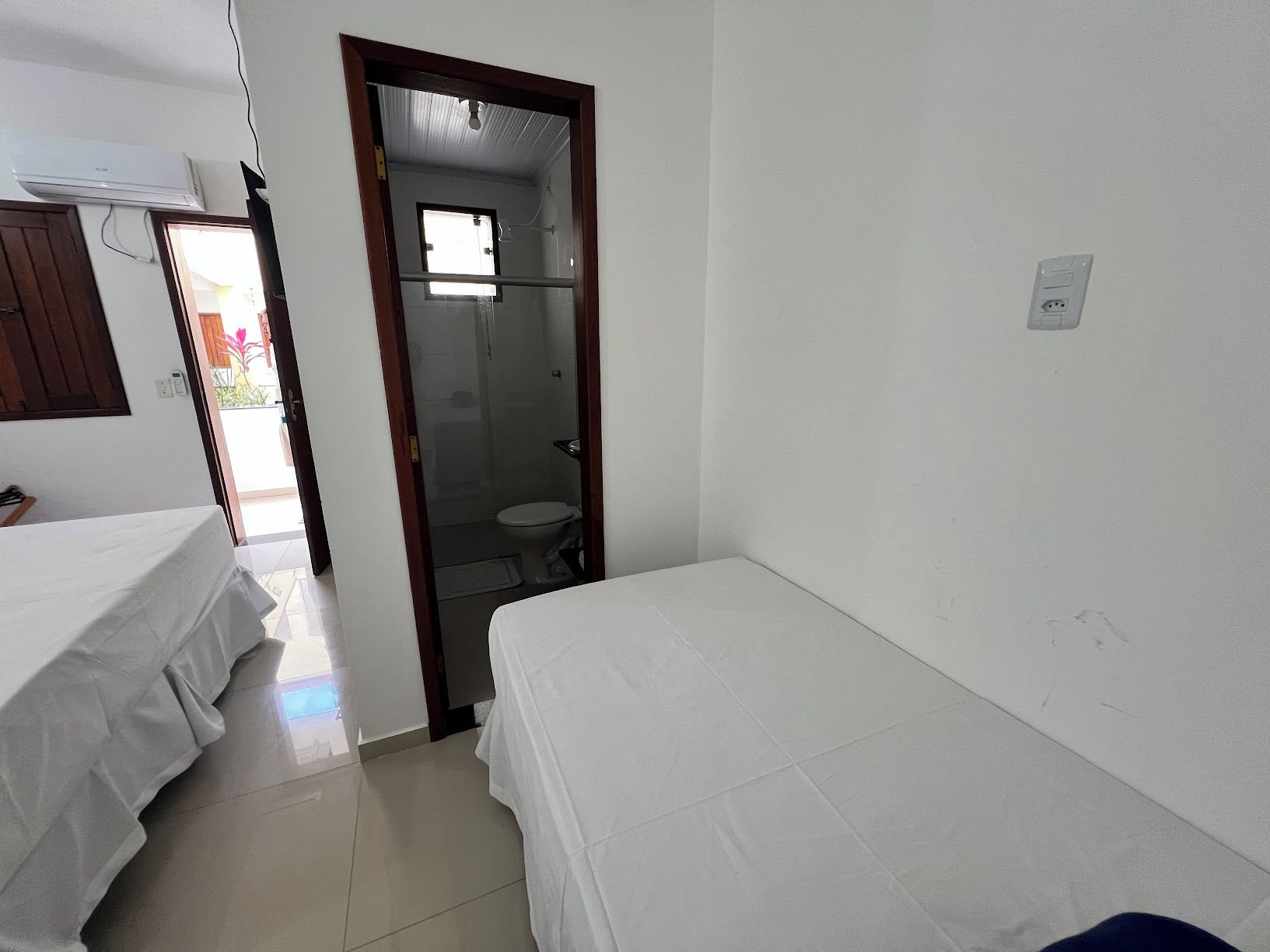 A room with two single beds, a bathroom with a toilet and shower, and a window providing natural light.