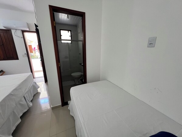 A room with two single beds, a bathroom with a toilet and shower, and a window providing natural light.