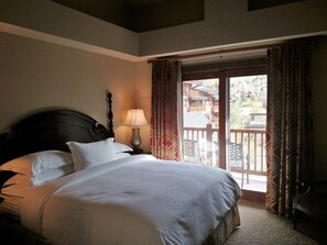 A hotel room with a large bed, a nightstand with a lamp, and a view of a balcony with a wooden railing. - Hilton Sunrise Lodge 2BR ski-in/ski-out condo in Canyons Village, Park City (Park City)