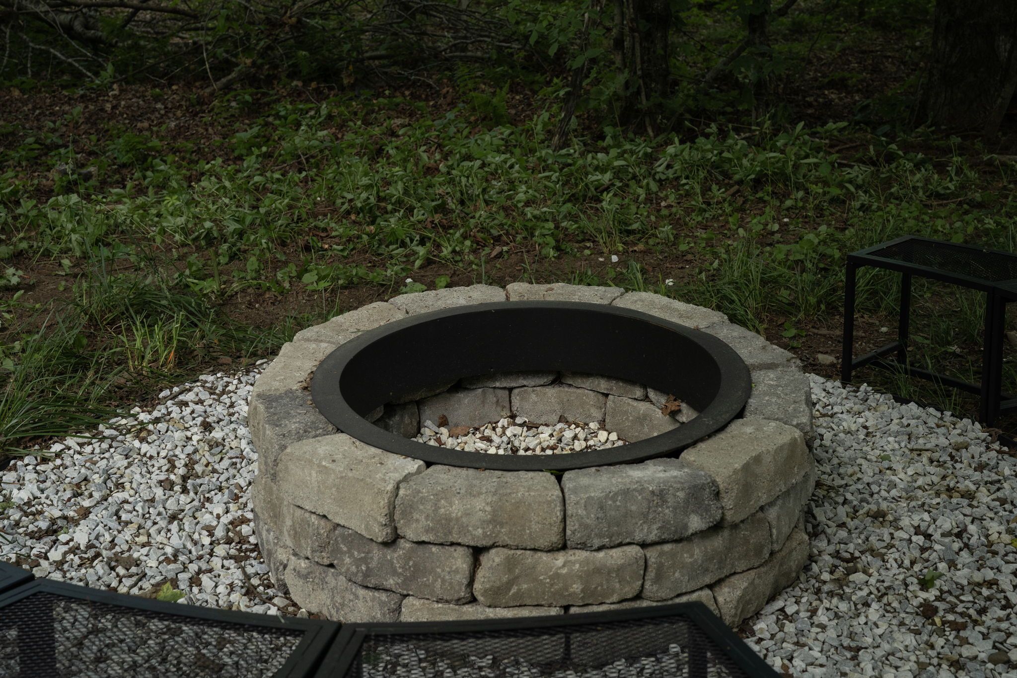 A stone fire pit with a metal rim, surrounded by gravel.