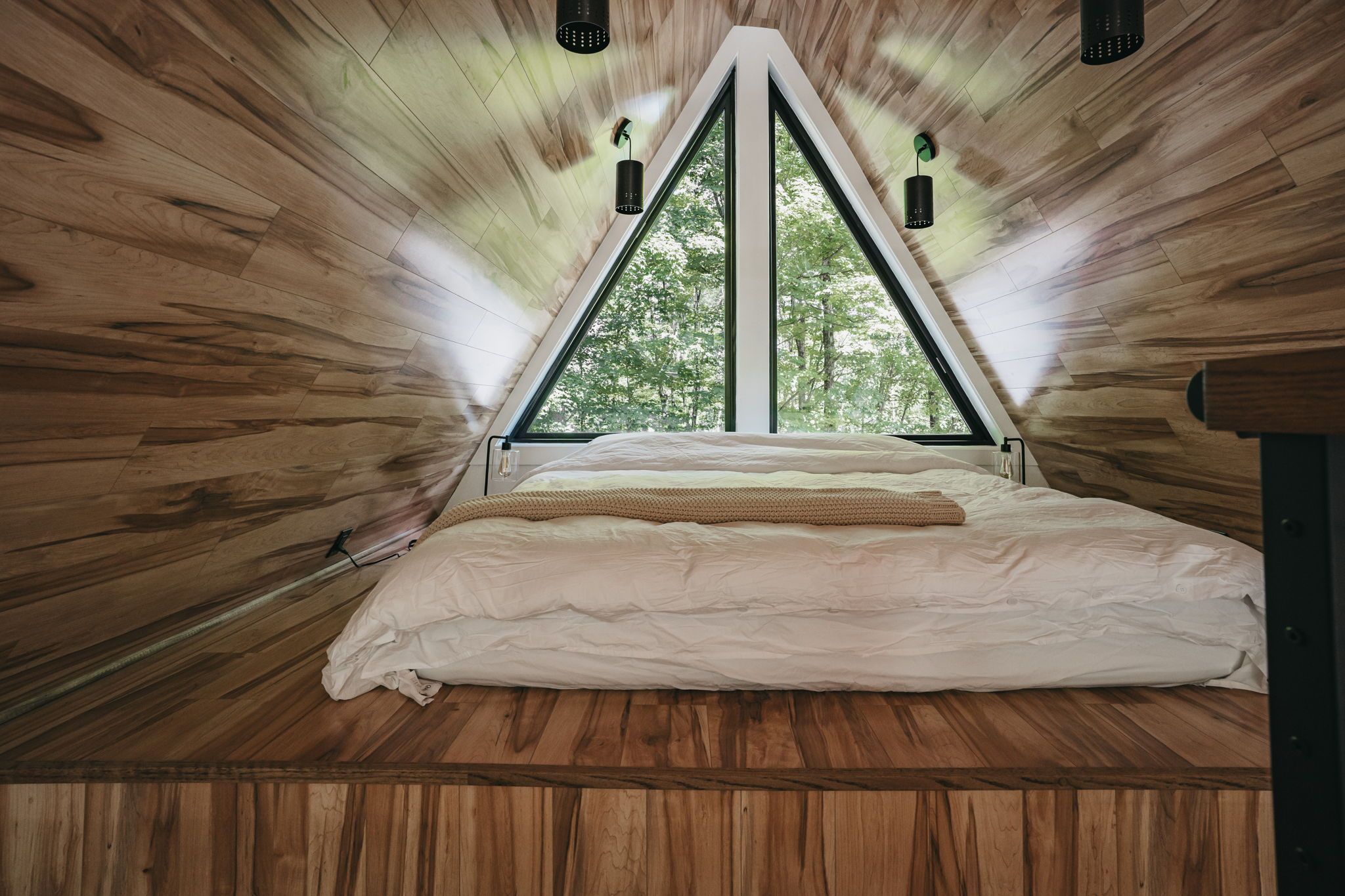 Ein Zimmer mit schrägem Dach, einem Bett mit weißer Bettwäsche und zwei Pendelleuchten.