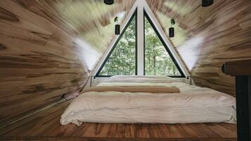 Ein Zimmer mit schrägem Dach, einem Bett mit weißer Bettwäsche und zwei Pendelleuchten.