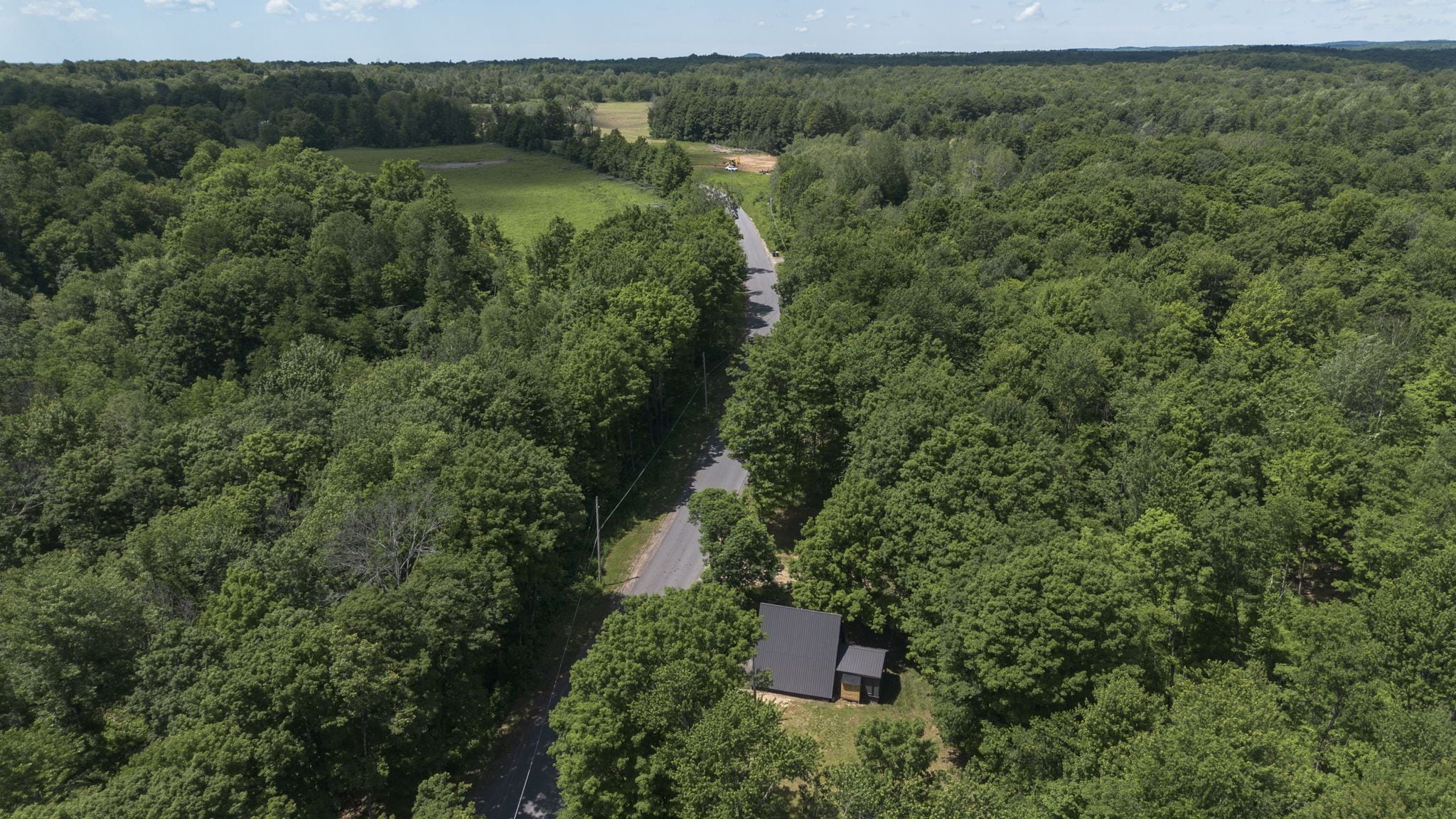 An aerial view of a forested area with a road and a small building.