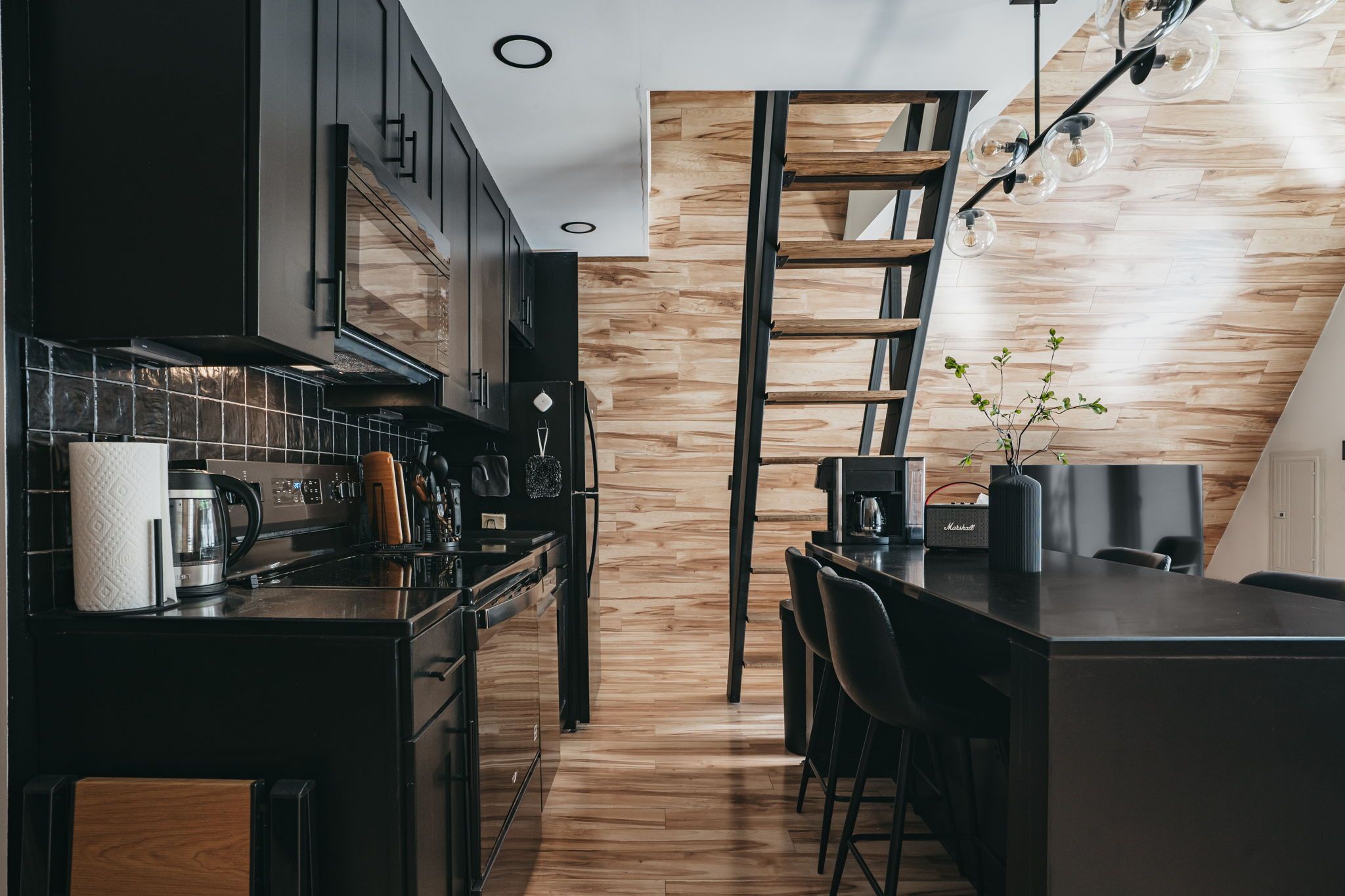 Eine moderne Küche mit dunklen Schränken, einer Holz-Akzentwand und einer eingebauten Leiter.