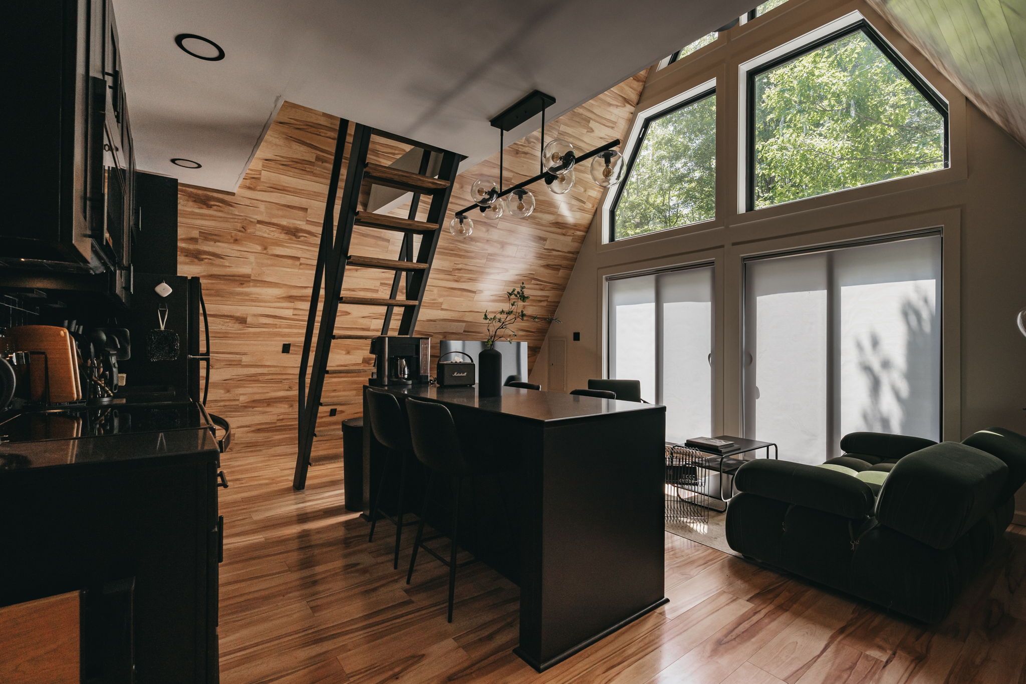 Eine moderne Küche mit Holzboden, einer zentralen Kochinsel und einem Essbereich mit einer schwarzen Sofaecke.