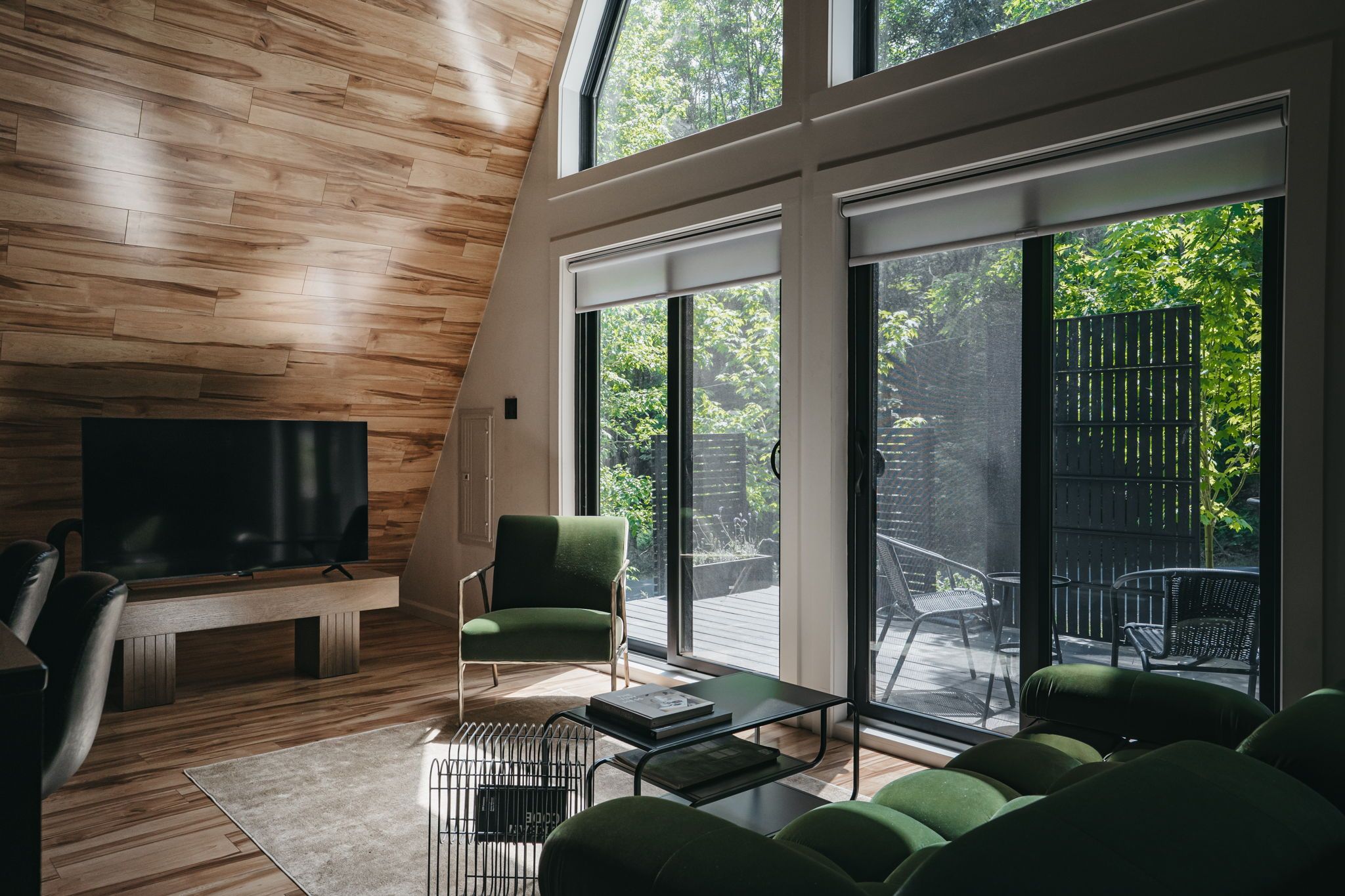 A modern living room with a television, green upholstered furniture, a fireplace, and large sliding glass doors leading to an outdoor patio.