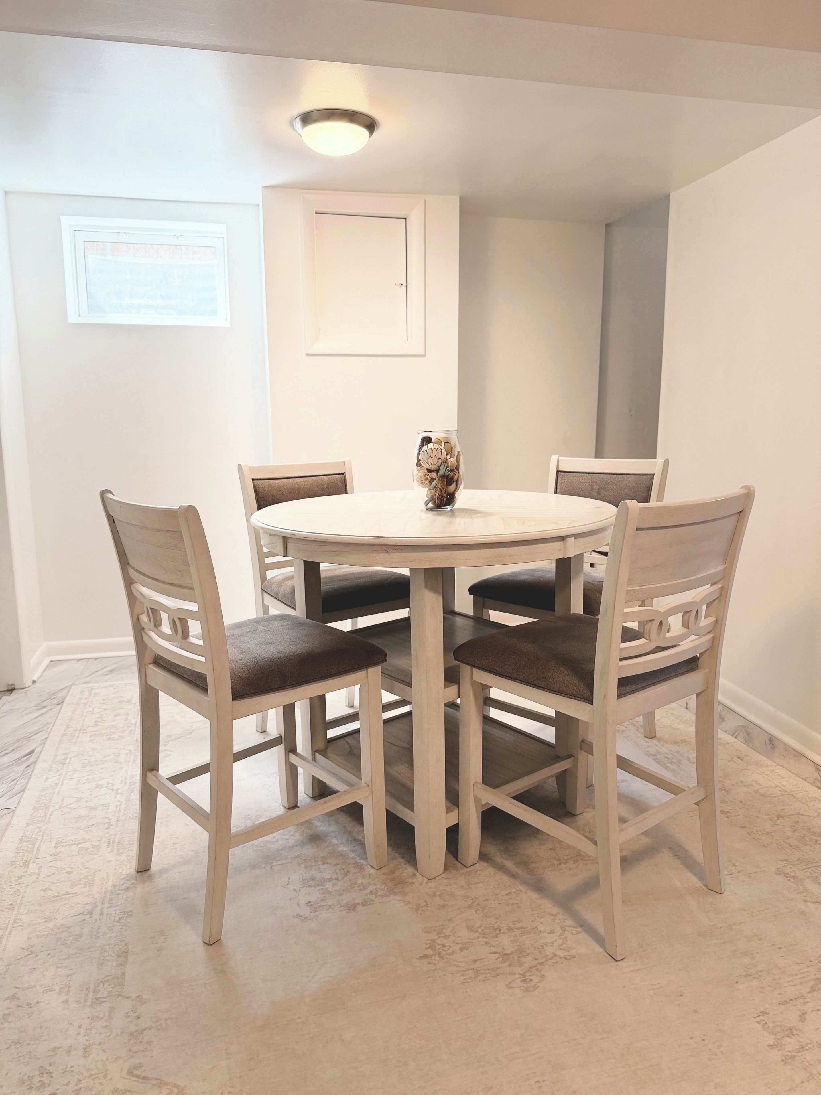 A dining area with a round table and four chairs, a vase with decorative items, and a ceiling light fixture.