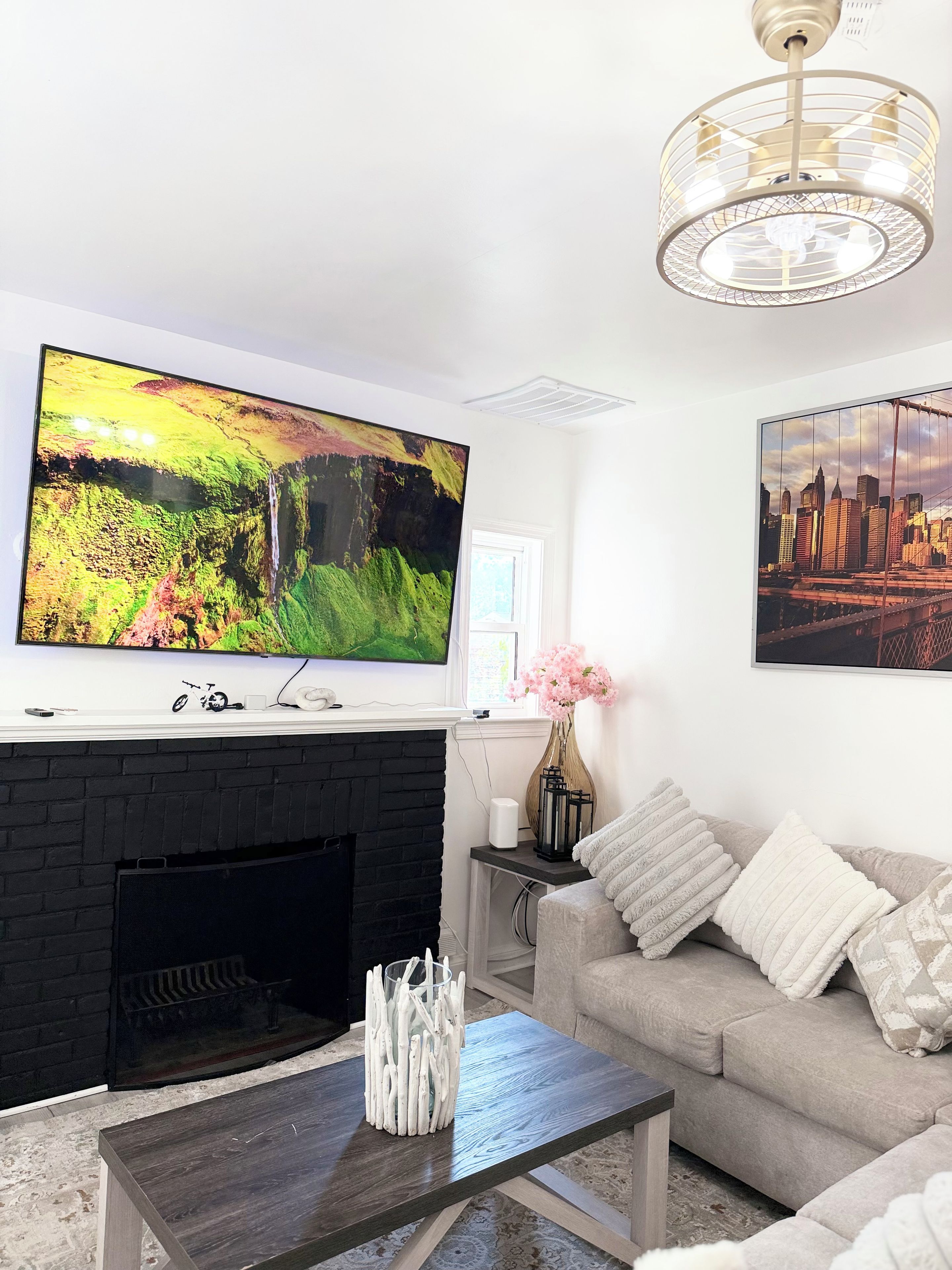 A living room with a flat-screen TV mounted above a fireplace, a sofa, a coffee table, and a chandelier.